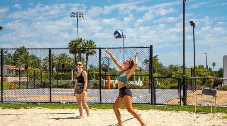 Student serves while playing volleyball at Pitzer College's beach volleyball court.